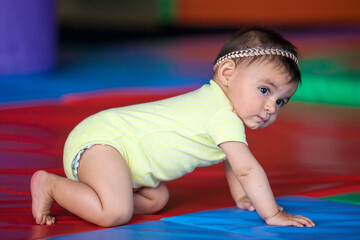 Wall Mural - Beautiful ten months baby girl crawling on a colorful background. Early stimulation for toddlers concept.