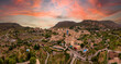 Aerial photograph of the historic city of Valldemoss, Sunset in Spain, pink and orange skyline, City in the mountains, Mallorca, Valldemossa, Mediterranean Sea, Cloudy sky, Panorama view at old town
