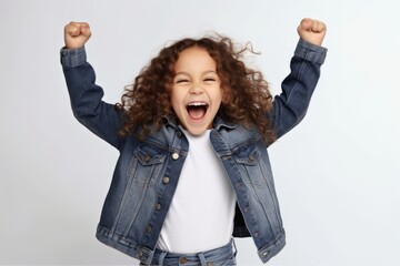 Wall Mural - Portrait of excited little girl with curly hair in denim jacket screaming and clenching fists over white background