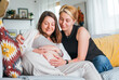 Young woman tender touching partner's female pregnant belly. Same-sex marriage couple on home living room sofa.  Woman's health, happy pregnancy doula supporting and calm mental mood concept image