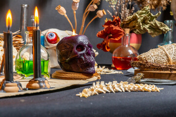 Human skull candle selective focus, arranged with black candles and spell potion vials on witchcraft background. Magic tools and items. Occult and esoteric concept. Magic chemistry and witch craft.