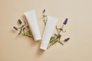 Wall Mural - Over beige background, two white tubes are displayed with lavender flower. Mockup of skin care cosmetic tube of beauty facial extracted from Lavender (Lavandula)