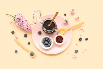 Board with jar of sweet jam and fresh blueberries on beige background