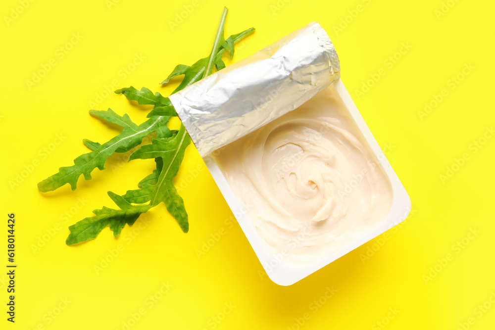 Plastic container with tasty cream cheese on yellow background