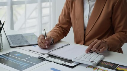 Wall Mural - Asian businesswoman working in the office, calculating financial reports, organizing paperwork using a laptop and calculator as an aid. management concept accounting.	
