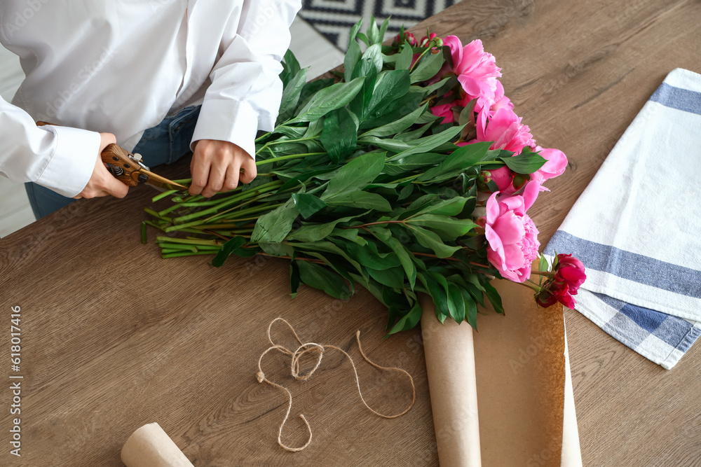 Young woman cutting peony flowers at table in kitchen, closeup