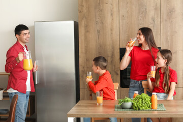 Happy parents with their little children drinking orange juice in kitchen