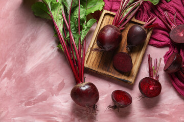 Wooden board of fresh beets with green leaves on pink background