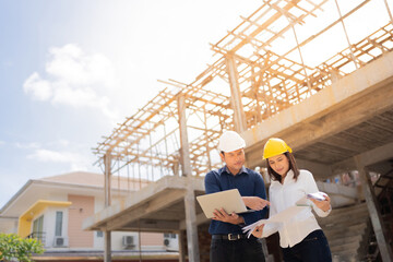 Two male and female engineers, mechanics, pointing to blueprints. There are tablets and drawings about construction architecture. It's on an industrial site project. Wear helmets and uniforms.