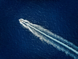 Wall Mural - high aerial view of a motor speeboat traveling over blue ocean and leaving a trail of fom and bubble