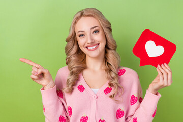 Poster - Photo of young marketer woman blonde hair direct finger novelty hold paper red love heart like picture isolated on green color background