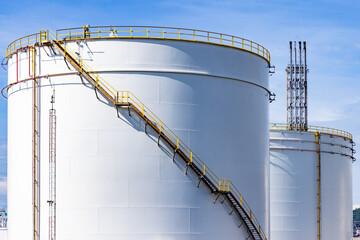 Wall Mural - White oil storage fuel tanks at depot station with access ladder against a blue sky. Vertical fuel tank staircase.Oil and gas industry.curve line spiral staircase on storage fuel tank.Oil industry,