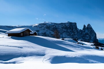 Poster - Snowy winter landscape featuring a small snow-covered house and distant mountains in the background.