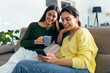 © nenetus - Two smiling young women talking while watching smartphone sitting on couch in the living room at home.