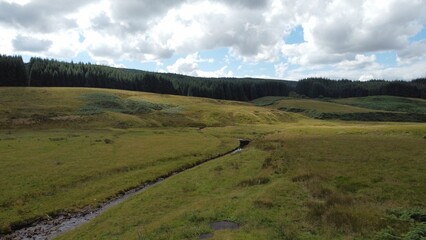 Poster - Scenic landscape featuring rolling hills surrounded by lush green trees and a winding stream