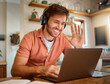 © HockleyMedia/peopleimages.com - Wave, laptop and online meeting with man in kitchen for video call, remote work and virtual communication. Happy, hello and social media with person at home for technology, streaming and entrepreneur