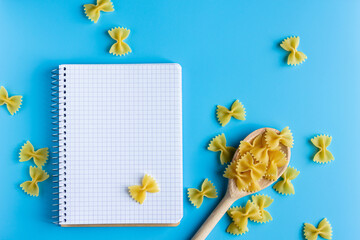 Canvas Print - Raw pasta farfalle with copy space on notebook on blue background