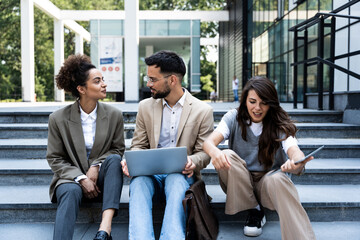 Wall Mural - Business people outdoor meeting. Company staff businessmen and businesswomen in suits are sitting on the steps of the stairs. Working break. Teamwork and brainstorming. Successful managers and team