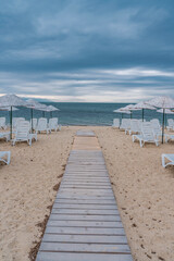 Wall Mural - Sun bed chairs with matress and straw beach umbrellas on beach. Blue hour time background by the sea..