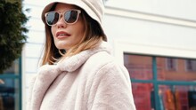 Outdoor Fashion Portrait Of Young Beautiful Smiling Lady Wearing Trendy White Faux Fur Coat. Stylish Woman Posing In The Street In Winter. Cheerful And Happy Model In Panama And Sunglasses