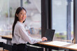 © Tj - Sharing good business news. Attractive young businesswoman talking on the mobile phone and smiling while sitting at her working place in office and looking at laptop PC.