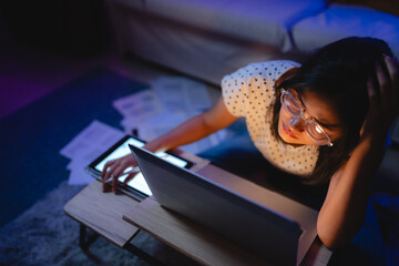 Wall Mural - Asian business women freelance working hard by using laptop computer, tablet, and document paper overtime in living room at house. Night overload entrepreneur job with online remotely work at home