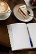 © Anna - A mug of cappuccino, a slice of cake and a notebook on the table in a cafe.
