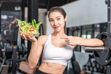 Young Asian woman wearing sportswear holding salad for breakfast before exercising in the gym. Healthy fitness concept