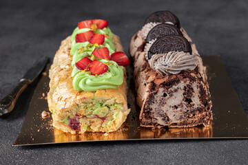 Two meringue rolls with strawberries and pistachios, as well as chocolate roll with cookies on gray background, close-up