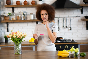 African american woman holding pregnancy test with worried expression at home