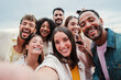 © Jose Calsina - Big group of young adult happy friends smiling taking a selfie portrait and looking at camera with friendly expression. A lot of cheerful multiracial people celebrating and laughing. Buddies bonding