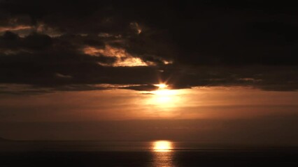 Wall Mural - Sunlight shines through clouds on a warm lit sky over large body of water.
