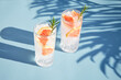 A chilled cocktail with fresh grapefruit slices and a sprig of rosemary under the shade of palm trees. Summer cold drinks. Soda with citrus