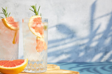 Wall Mural - A chilled cocktail with fresh grapefruit slices and a sprig of rosemary under the shade of palm trees. Summer cold drinks. Soda with citrus