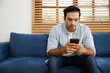 © offsuperphoto - young handsome man sitting on sofa and using smartphone at hone