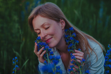 Wall Mural - Portrait of young woman with blue flowers in a field