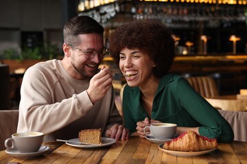 Canvas Print - International dating. Handsome man feeding his girlfriend with cake in cafe