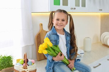 Canvas Print - Cute girl with yellow tulips and wicker basket full of Easter eggs in kitchen