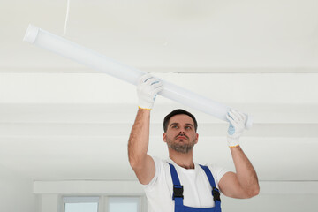 Poster - Electrician installing led linear lamp indoors. Ceiling light