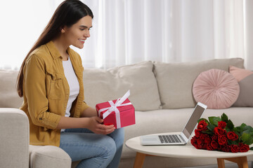 Wall Mural - Valentine's day celebration in long distance relationship. Woman holding gift box while having video chat with her boyfriend via laptop at home