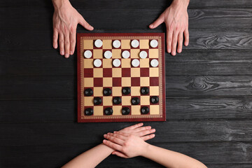 Canvas Print - Man playing checkers with woman at black wooden table, top view