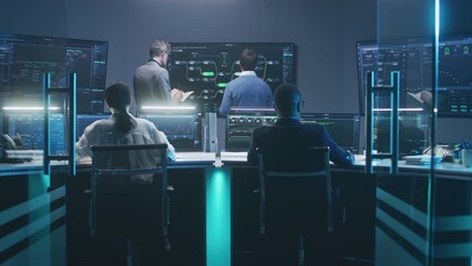 Diverse team of IT technical specialists and software managers work with database, real-time analysis charts and blockchain network on computers and big digital screens in monitoring office at night.