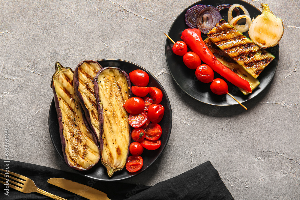 Plates with tasty grilled vegetables on grey background