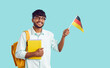 Young positive Indian man student Germany University with backpack and books waving political flag of Deutschland getting local education at state college stands on turquoise background