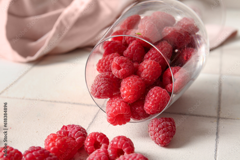 Glass with fresh raspberries on white tile background