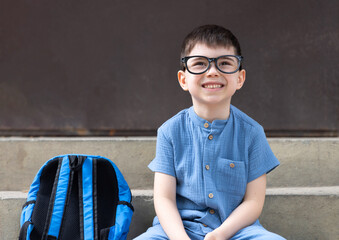 back to school.happy smiling preschooler boy kid with both raised hand hooray gesture or sitting on school stairs outside.child wearing glasses frame smart intelligent