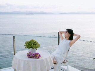 Sticker - East Asian female sitting at a table on a pier, overlooking a tranquil body of water