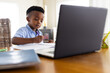 © Wavebreak Media - African american boy sitting at table and using laptop for online lesson