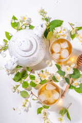 Wall Mural - Organic herbal health summer cold drink. Jasmine flowers green tea, in glass, with ice cubes, teapot, on white table, with blooming jasmine flowers 