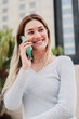 © Jose Calsina - Vertical portrait of young pretty young woman smiling and talking by a smartphone device. Happy blonde female having a mobile phone call conversation at city urban street. Girl using cellphone outside